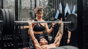 Man lifting weights with woman spotting in Mexico City gym. Urban and dynamic fitness scene.