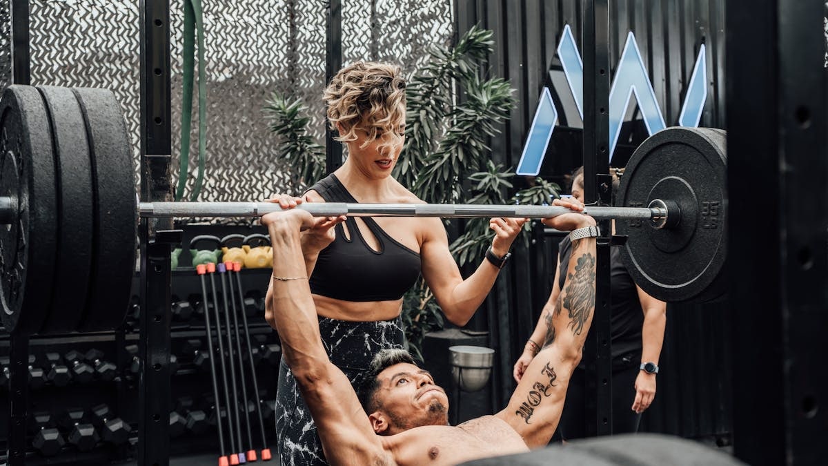 Man lifting weights with woman spotting in Mexico City gym. Urban and dynamic fitness scene.